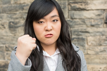Portrait of young aggressive woman in front of a stone wall looking angry and holding fistの写真素材