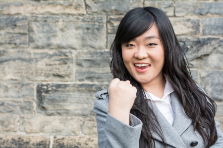 Portrait of successful young woman in front of a stone wall holding up fistの写真素材