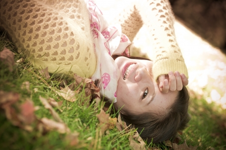 Young woman laying in grass with a bunch of fallen leafs, covering one eyeの写真素材
