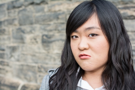 Portrait of young woman in front of a stone wall looking angryの写真素材
