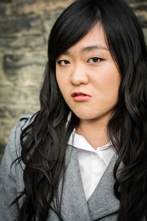Portrait of young woman in front of a stone wall looking angryの写真素材