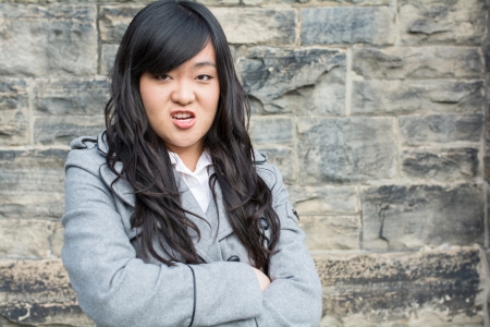 Portrait of young woman in front of a stone wall looking angry with arms crossedの写真素材