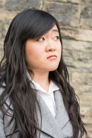 Portrait of young girl in front of a stone wall looking upset and looking awayの写真素材