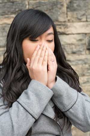 Portrait of young girl in front of a stone wall looking upset and covering mouthの写真素材