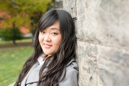 Portrait of young woman standing back against a stone wall looking innocentの写真素材