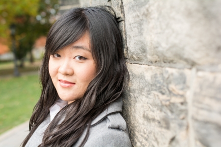 Portrait of young woman standing back against a stone wall looking innocentの写真素材