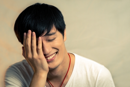 Young man covering his face and smiling, with fashion tone and backgroundの写真素材