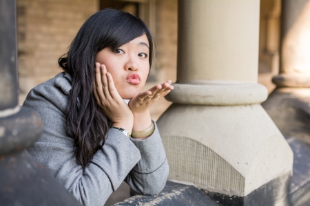 young woman leaning forward next to stone pillars blowing a kissの写真素材
