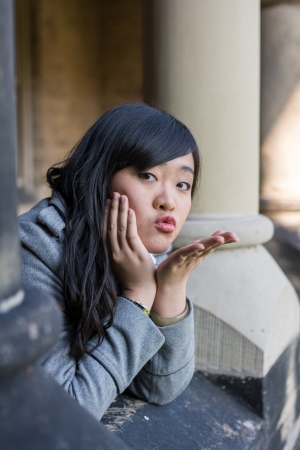 young woman leaning forward next to stone pillars blowing a kissの写真素材
