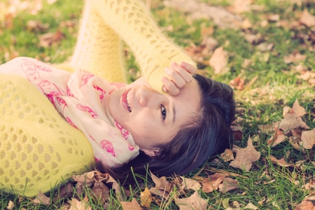 Young woman laying in grass with a bunch of fallen leafs, covering one eyeの写真素材