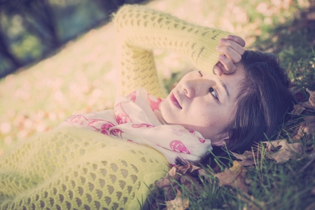 Young woman laying in grass with a bunch of fallen leafs, covering one eyeの写真素材