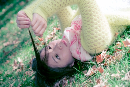 Young woman laying in grass with a bunch of fallen leafs, pulling her hairの写真素材
