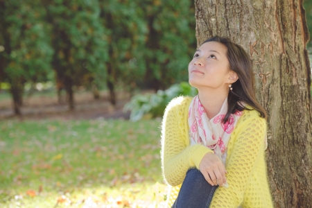 Portrait of happy looking woman sitting against a tree and looking upwardsの写真素材