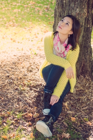 Portrait of happy looking woman sitting against a tree and looking upwardsの写真素材