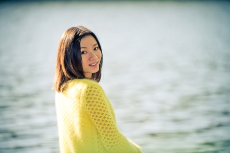 Portrait of young attractive woman sitting on a rock next to a river looking backの写真素材