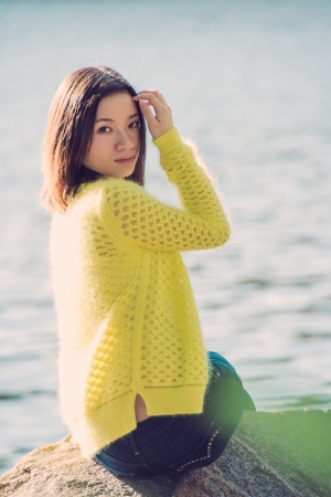 Portrait of young attractive woman sitting on a rock next to a river looking backの写真素材