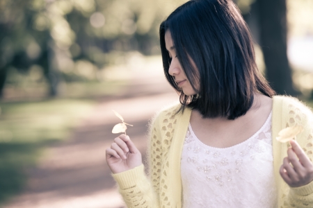 Cute young girl holding a handful of leafs at the end of a park roadの写真素材