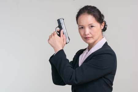 Portrait of woman in business suit holding a hand gun with agent pose on grey backgroundの写真素材