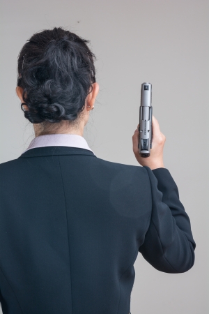 Back of woman in business suit holding a hand gun pointing upの写真素材