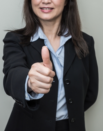 Professional woman in business suit giving thumbs up in approval on grey background の写真素材