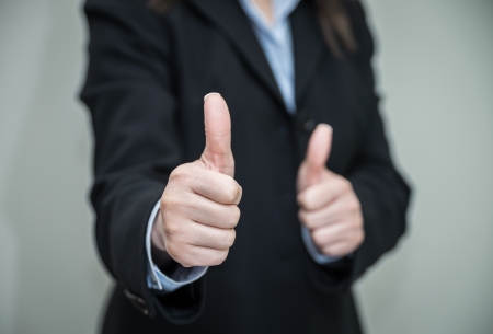 Professional woman in business suit giving thumbs up in approval on grey background の写真素材