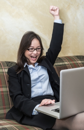Professional woman in business suit on sofa cheering with fists in air with laptop の写真素材