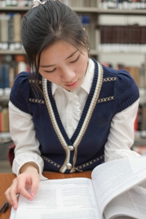 Portrait of young female student reading a textbook in front of library bookshelfの写真素材