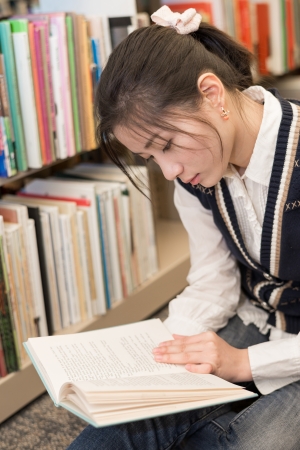Young attractive woman reading a book while sitting on the floor in front of a bookshelfの写真素材