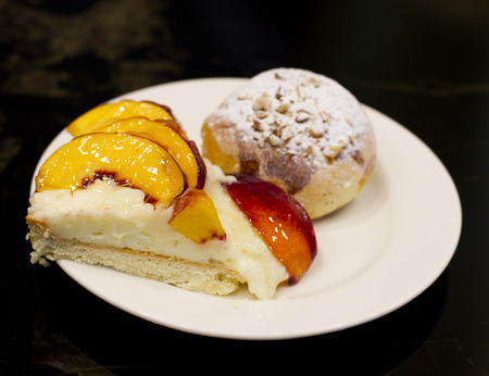 Bun with custard and powdered sugar. Peach pie in a glaze.