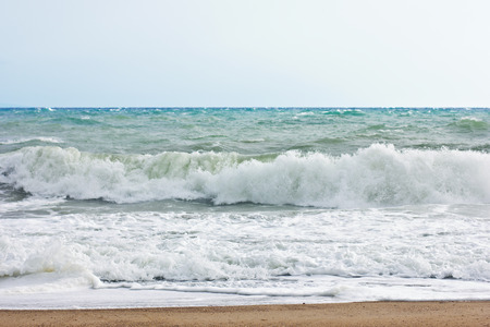 Stormy sea and blue sky, white sea foam on the yellow sandy beach.