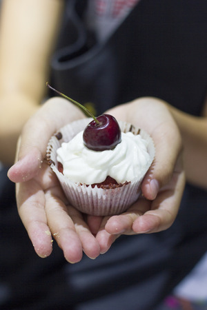 Cupcake "Red velvet" with white whipped cream and cherries in cook's handsの写真素材