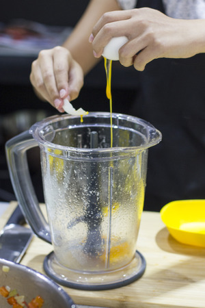 The cook breaks the raw egg into blender. Egg yolk flowing.の写真素材