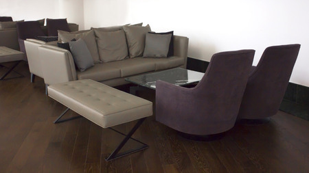 Business Interior. Brown parquet, beige leather sofas with cushions and a glass table