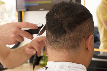 Back view of man getting short hair trimming at barber shop with a clipper machineの写真素材
