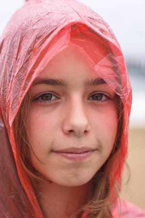 Portrait of pretty teenager girl in wet red raincoat under the rainの写真素材