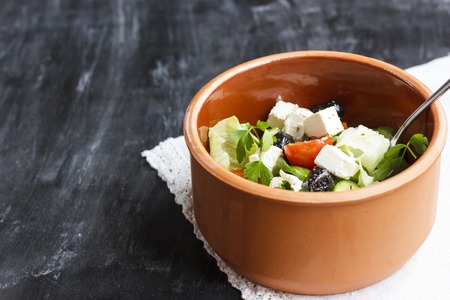 Vegetarian Greek salad with feta cheese, arugula, olives and cherry tomatoes and italian herbs in a clay bowlの写真素材