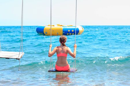 Happy smiling pretty young teenager girl on a swing in the blue seaの写真素材