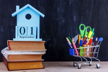 Set of colored pencils and markers for school in a shopping cart. 1 of September calendar on pile of booksの写真素材