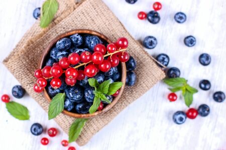 Fresh blueberries and red currants with mint leaves in wooden bowl on burlap. Diet food, vegan berriesの写真素材
