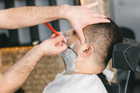 Hairdresser shaves a beard to a man with a razor in a barbershopの写真素材