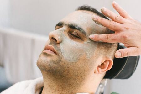 Male skin care in the beauty salon. Applying clay cleansing mask on a man's faceの写真素材