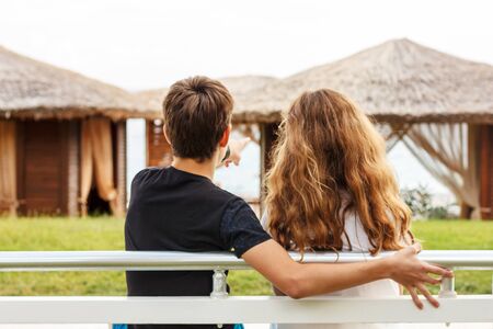The guy hugs a girl sitting on a bench next to each other and looking at the seaの写真素材