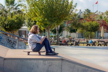 Girl teenager sitting on a skateboard. Beautiful fashionable skateboarder in jeans and a hoodie on ramp.の写真素材
