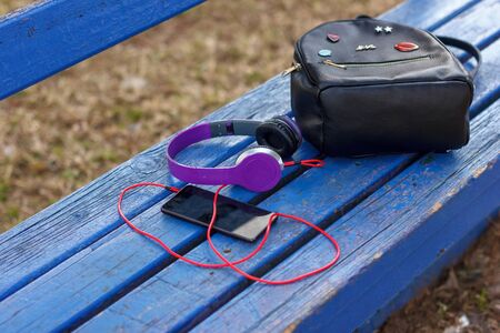 Headphones with smartphone and a black backpack on a blue park bench