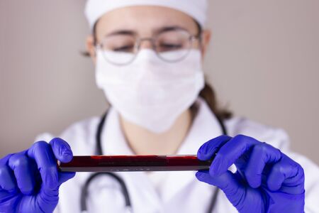 Nurse with respirator mask holding tube with blood test result for coronavirusの写真素材