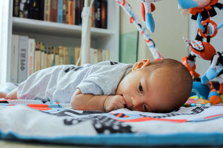Cute little baby on the play mat with toys. Serious infant with finger in his mouthの写真素材