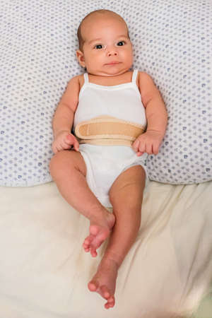 Baby in an umbilical hernia bandage. Sweet infant on the bed