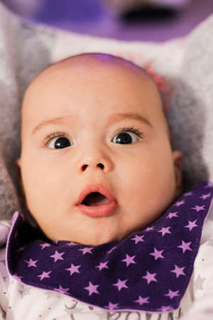 Portrait of cute baby close-up. Sweet little infant looks surprised. Bald baby with brown eyes and...