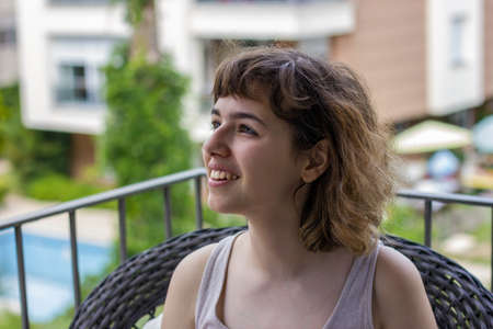 Young pretty curly girl smiling on balcony of apartmentの写真素材