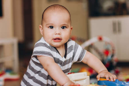 Cute chubby baby stands and plays with children's music table. Lots of colorful toys everywhere.の写真素材